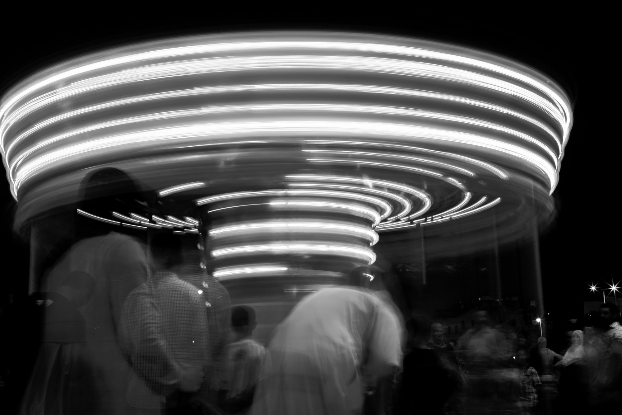 Long-exposure photograph of a fairground carousel at night, its lights drawn into bright concentric streaks against deep black.