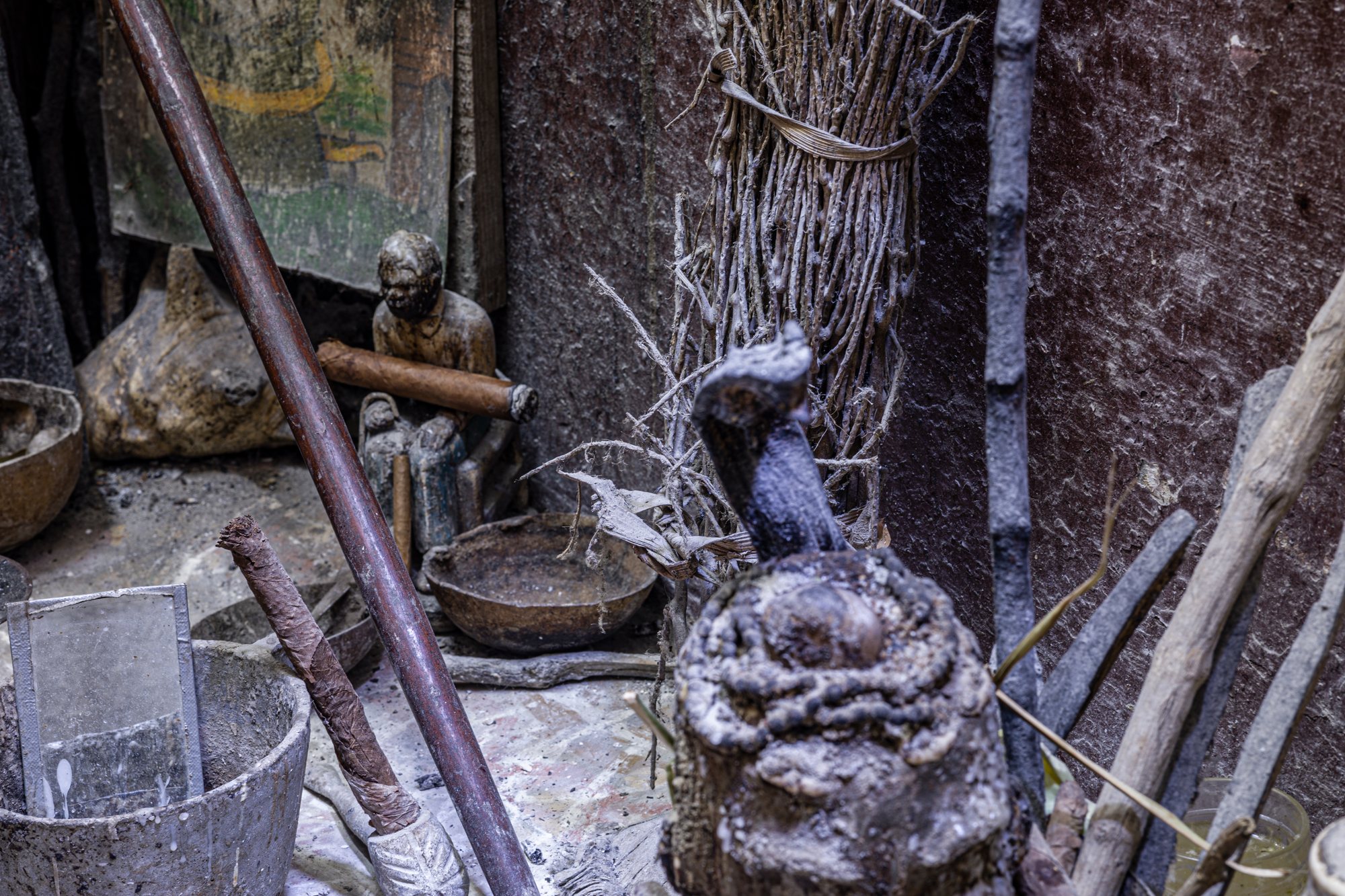 A crowded domestic altar: a statue, a stone head, feathers, and ritual bundles