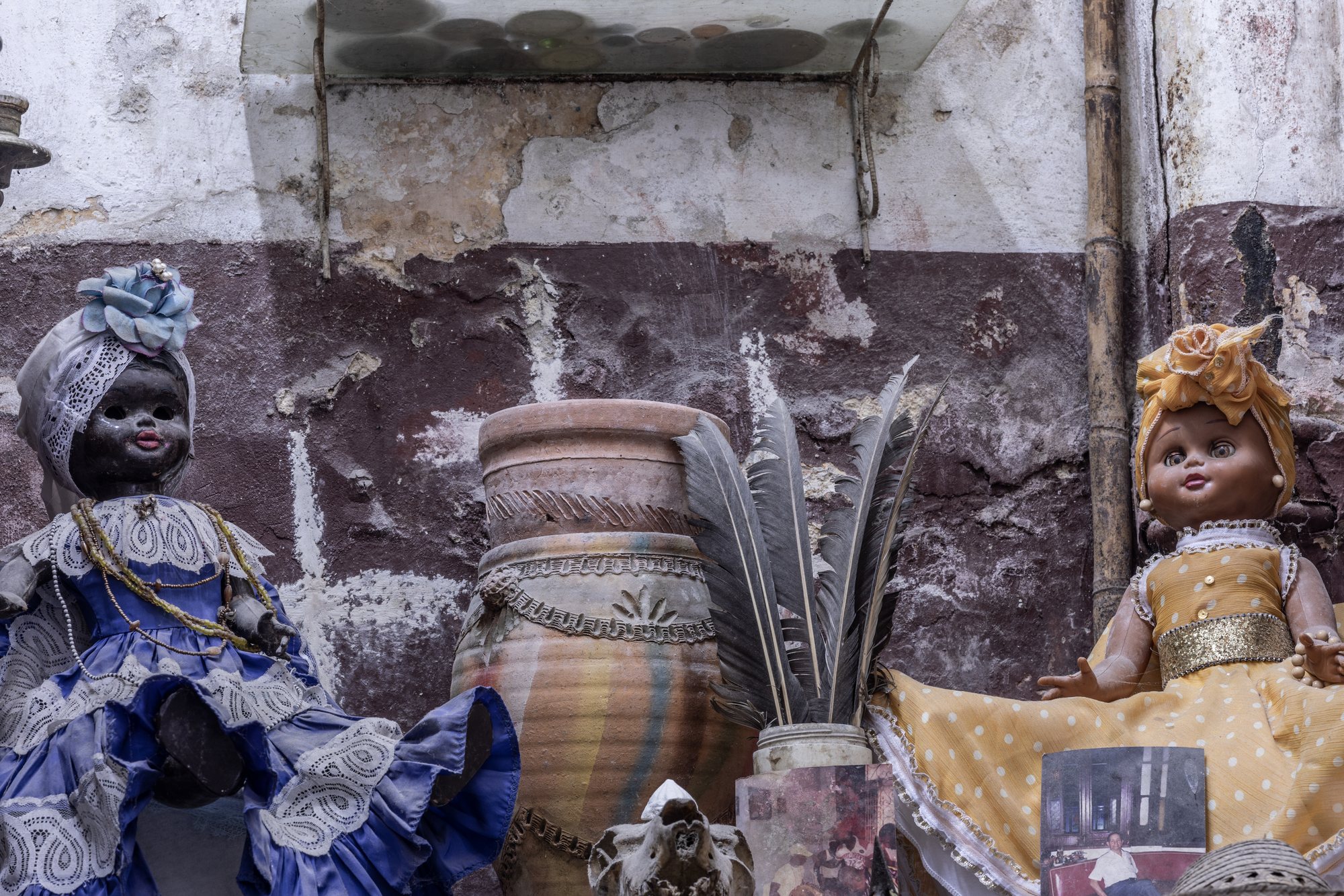 Two Orisha dolls - Yemayá in blue, Ochún in yellow - on a peeling wall altar