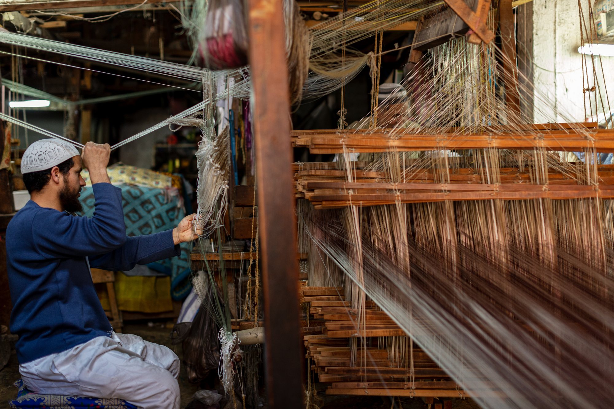 A weaver at the loom, threads drawn tight by hand