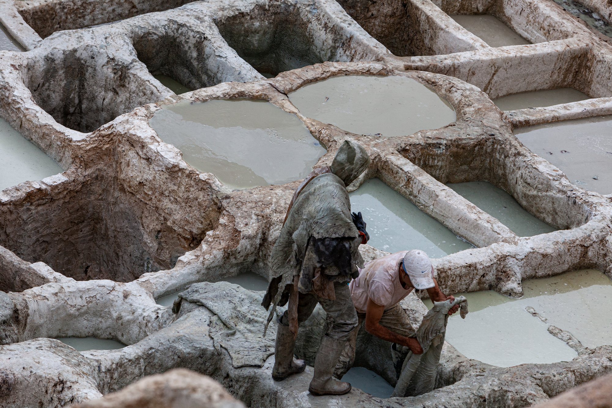 Two tanners lift a soaked hide from a stone pit