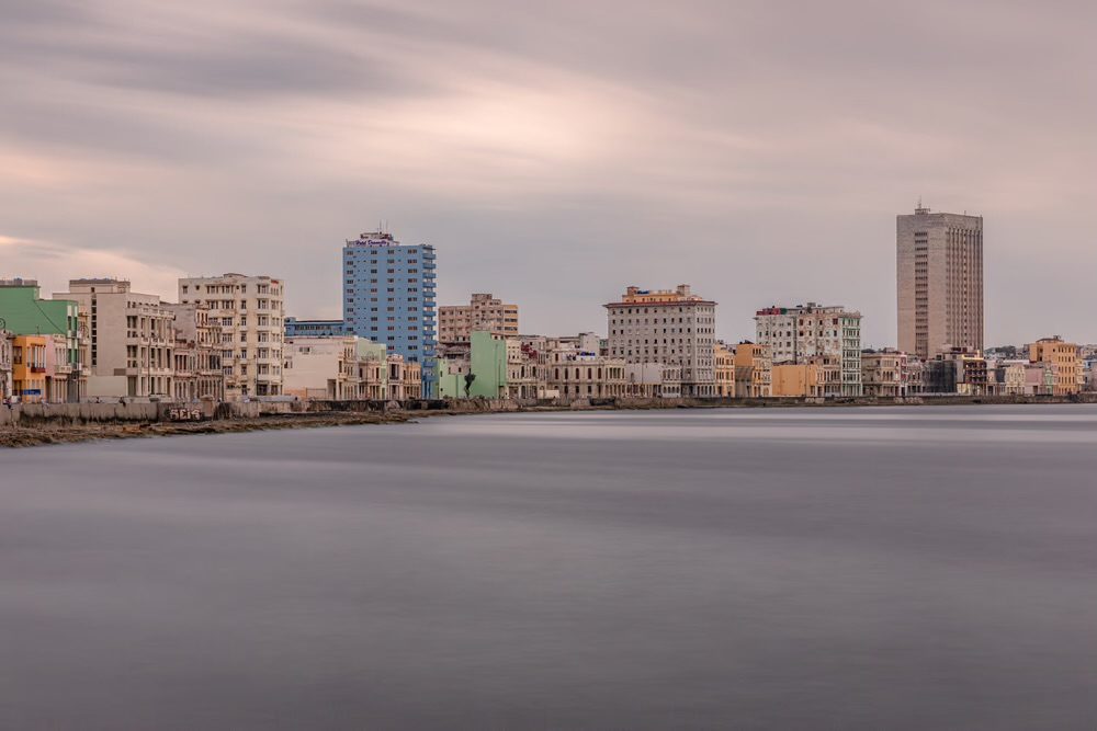 A long-exposure view of the Havana skyline along the Malecón, the blue FOCSA building and weathered pastel waterfront facades under a soft sky