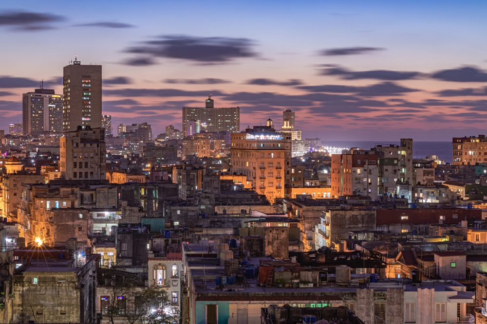 A long-exposure twilight panorama of the Havana skyline, the FOCSA building and Hotel Nacional tower against purple clouds and the Caribbean