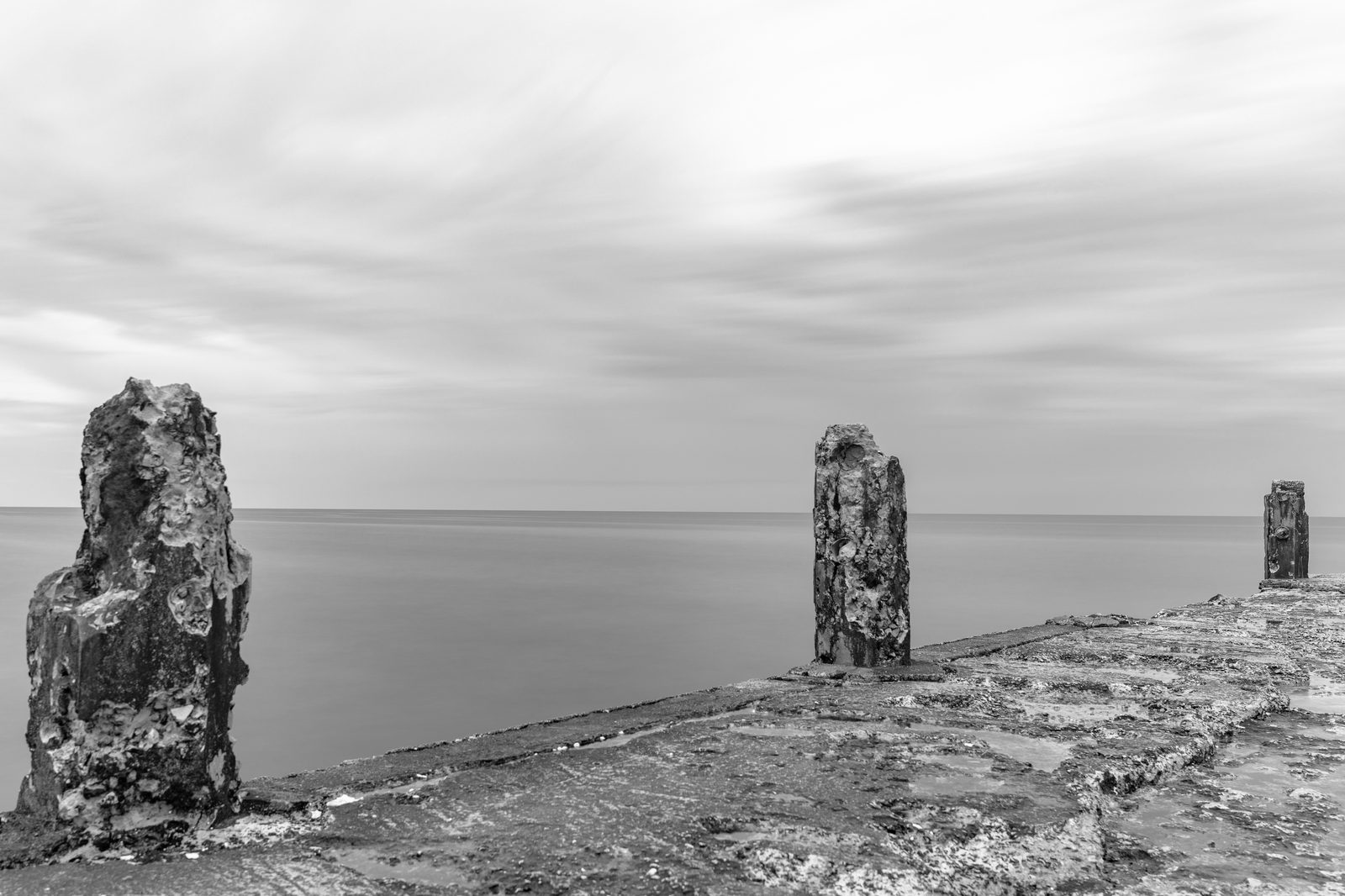 Monolith II - weathered concrete monoliths standing on a crumbling pier, receding into a calm grey sea