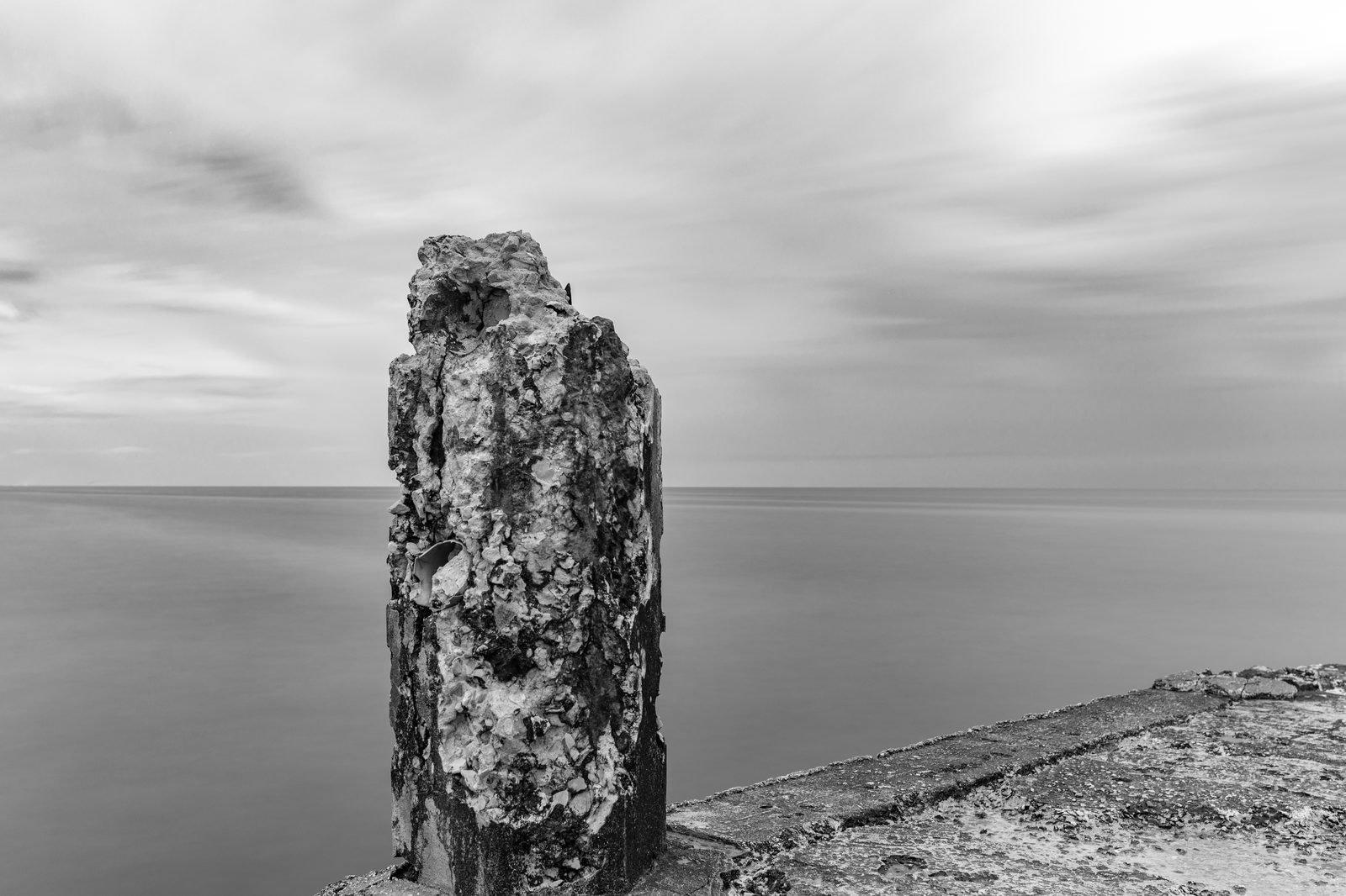 Monolith III - a solitary eroded concrete monolith on the edge of a crumbling pier, its pitted surface against long-exposure water