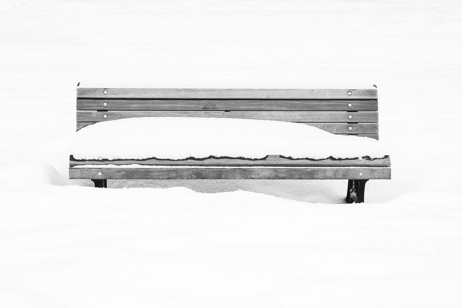 A snow-laden wooden park bench against a vast, minimalist white winter field