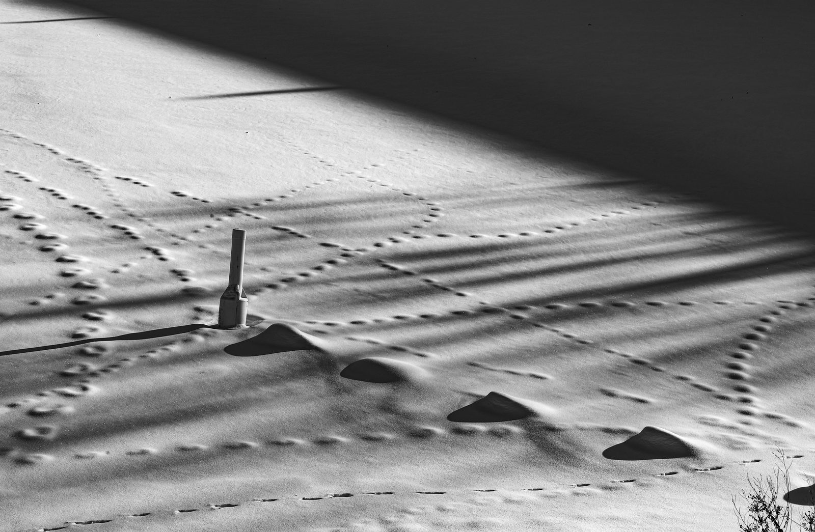 A solitary white post and snow drifts amid a chaotic network of footprints on textured snow