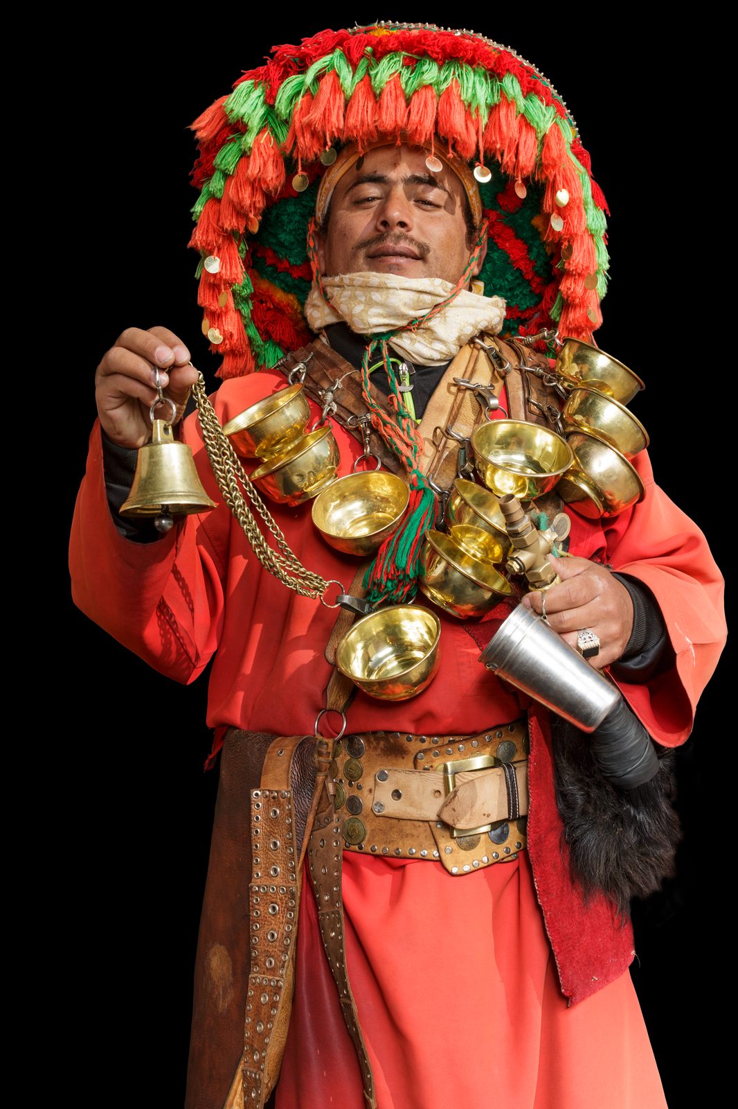 A Moroccan Boujou musician in a towering red-and-green yarn hat, a harness of brass bowls and a bell
