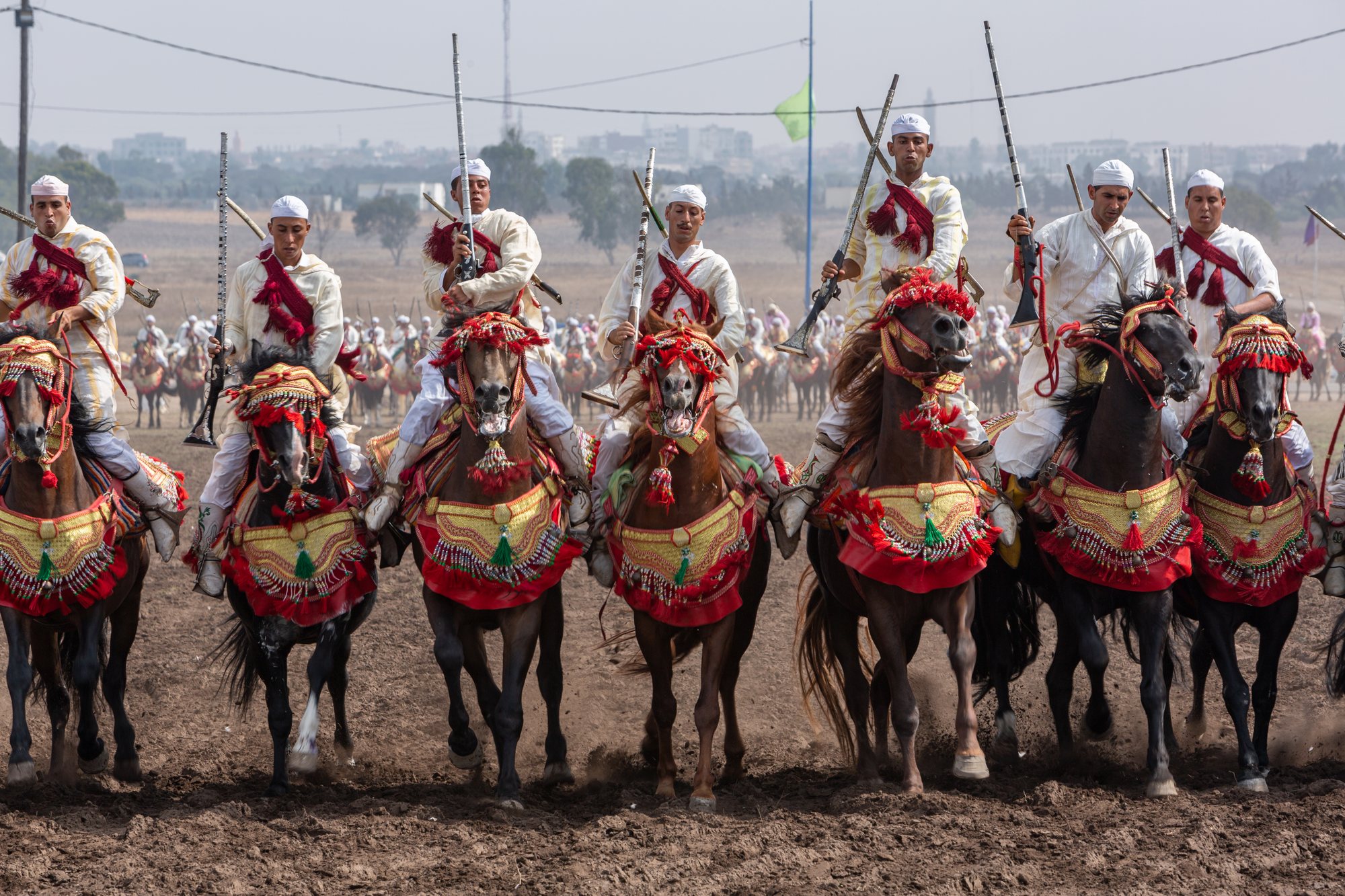 A line of white-robed riders charging in unison across a dusty field