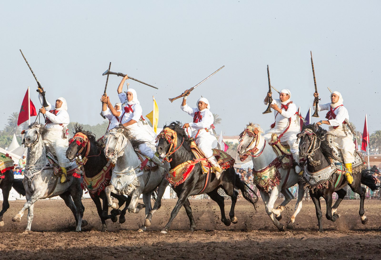 A tight line of riders galloping past the festival fence, rifles raised, dust trailing